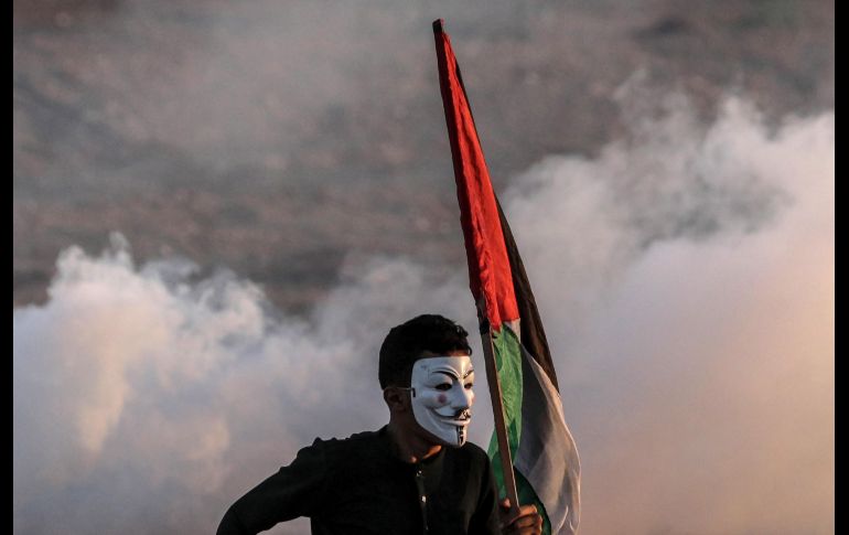 Un palestino con una máscara de Guy Fawkes ondea la bandera nacional durante los disturbios cerca de la frontera marítima entre Israel y Gaza. Los palestinos exigen el derecho de regresar a casa de los compatriotas refugiados que tuvieron que abandonar sus hogares desde que se desencadenara la guerra en 1948 con la creación del estado israelí. EFE/ M. Saber