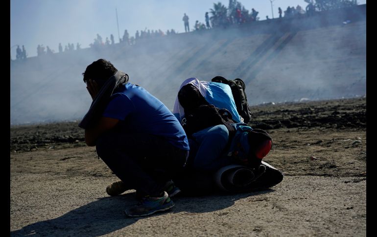 Tres hondureños en Tijuana se cubren del gas lacrimógeno lanzado por autoridades estadounidenses cerca del cruce fronterizo de El Chaparral.