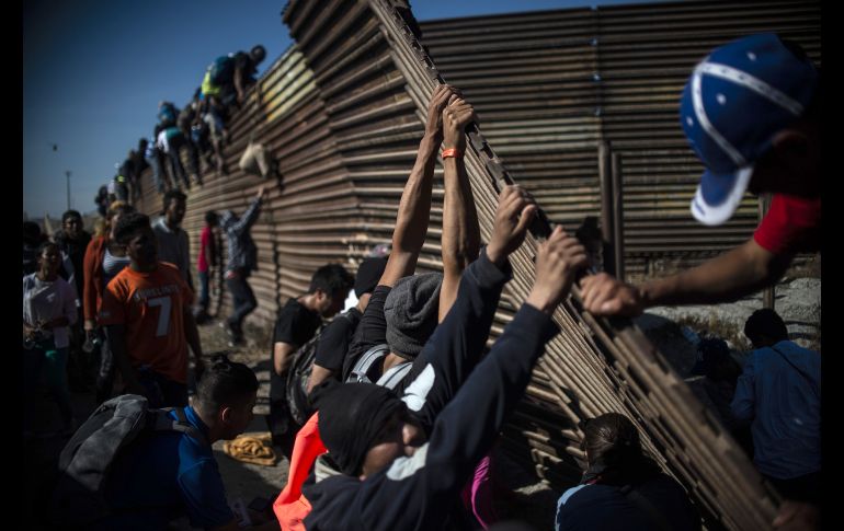 Migrantes intentan cruzar una valla cerca del cruce de El Chaparrral. AFP/P. Pardo