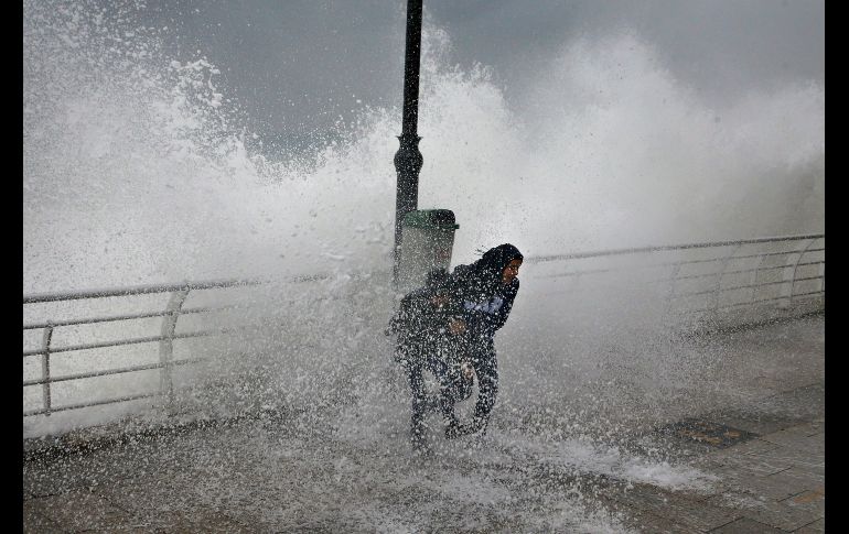 Una mujer y su hijo juegan mientras una ola se estrella en un rompeolas en Beirut, Líbano. Una fuerte tormenta dejó bajas temperaturas e intensas lluvias en la costa del país. AP/B. Hussein