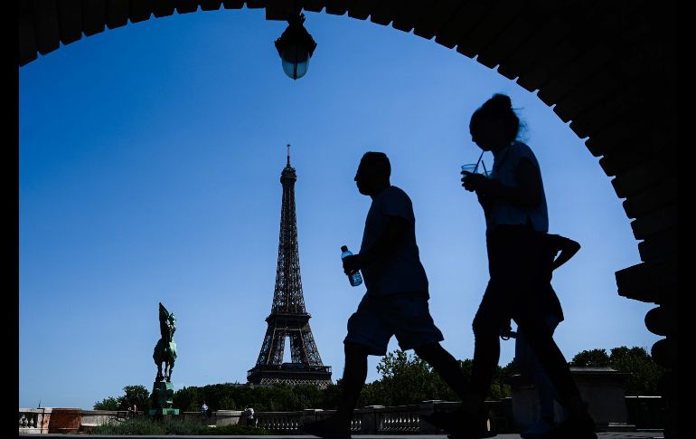 Personas llevan bebidas mientras caminan frente a la torre Eiffel en París. Este jueves se podría batir el récord histórico de calor registrado en la capital francesa, con 41°C. AFP/P. Lopez