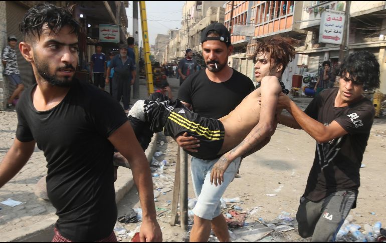 Jóvenes cargan a un manifestante herido durante enfrentamientos con policías en Bagdad. AFP/A. Al-Rubaye