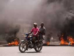 Dos hombres en motocicleta pasan frente a una barricada en llamas durante una jornada de protestas en Cap-Haitien, Haití. EFE/O. Barría