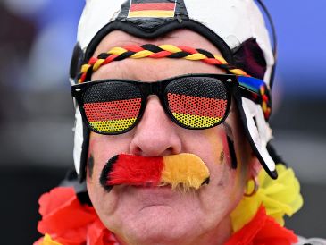 Aficionado de Alemania viste ropa con los colores de su país mientras espera el inicio del partido inaugural de la Euro 2024 en la zona de aficionados cerca de la histórica Puerta de Brandenburgo. AFP / R. Hirschberger