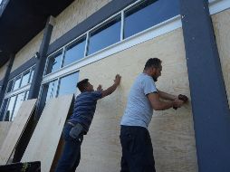 Empleados de una tienda de muebles cubren las ventanas con tablones ante de la llegada del huracán 
